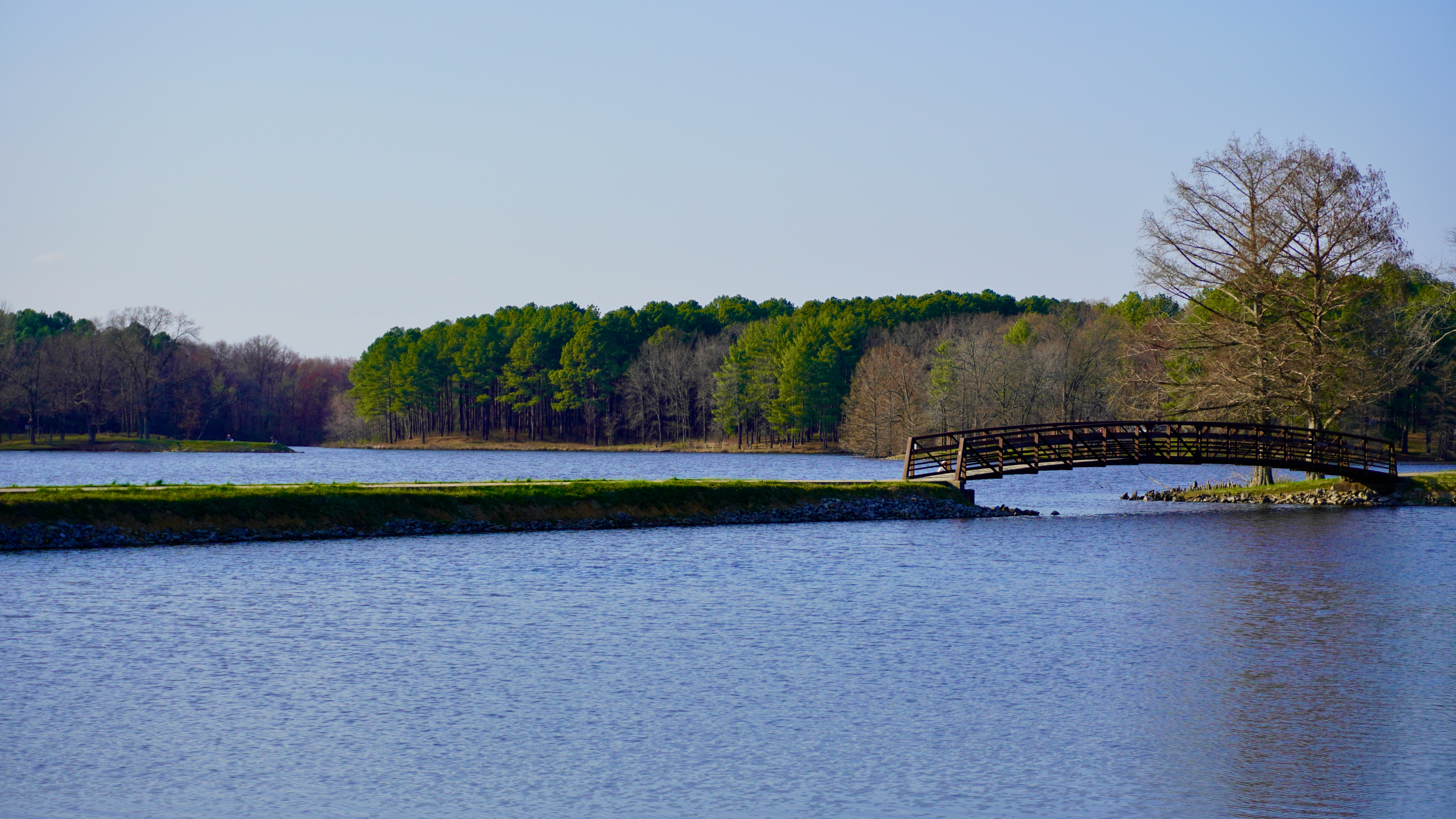 a bridge and blue water of a lake against the background of pine trees in hamilton county state fish and wildlife area