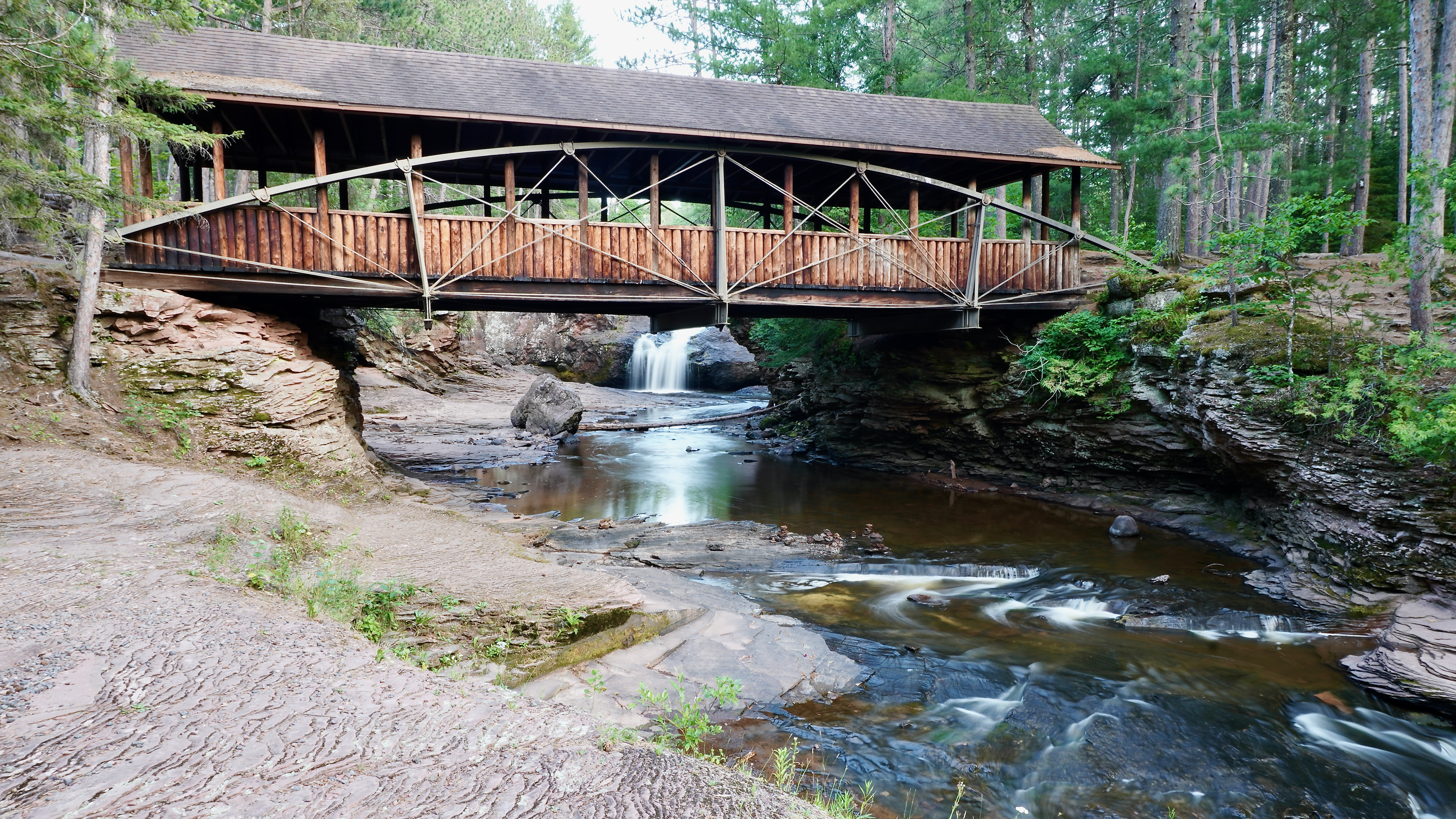 a brown wooden bridge over a rocky Amnicon river with the fall in the background