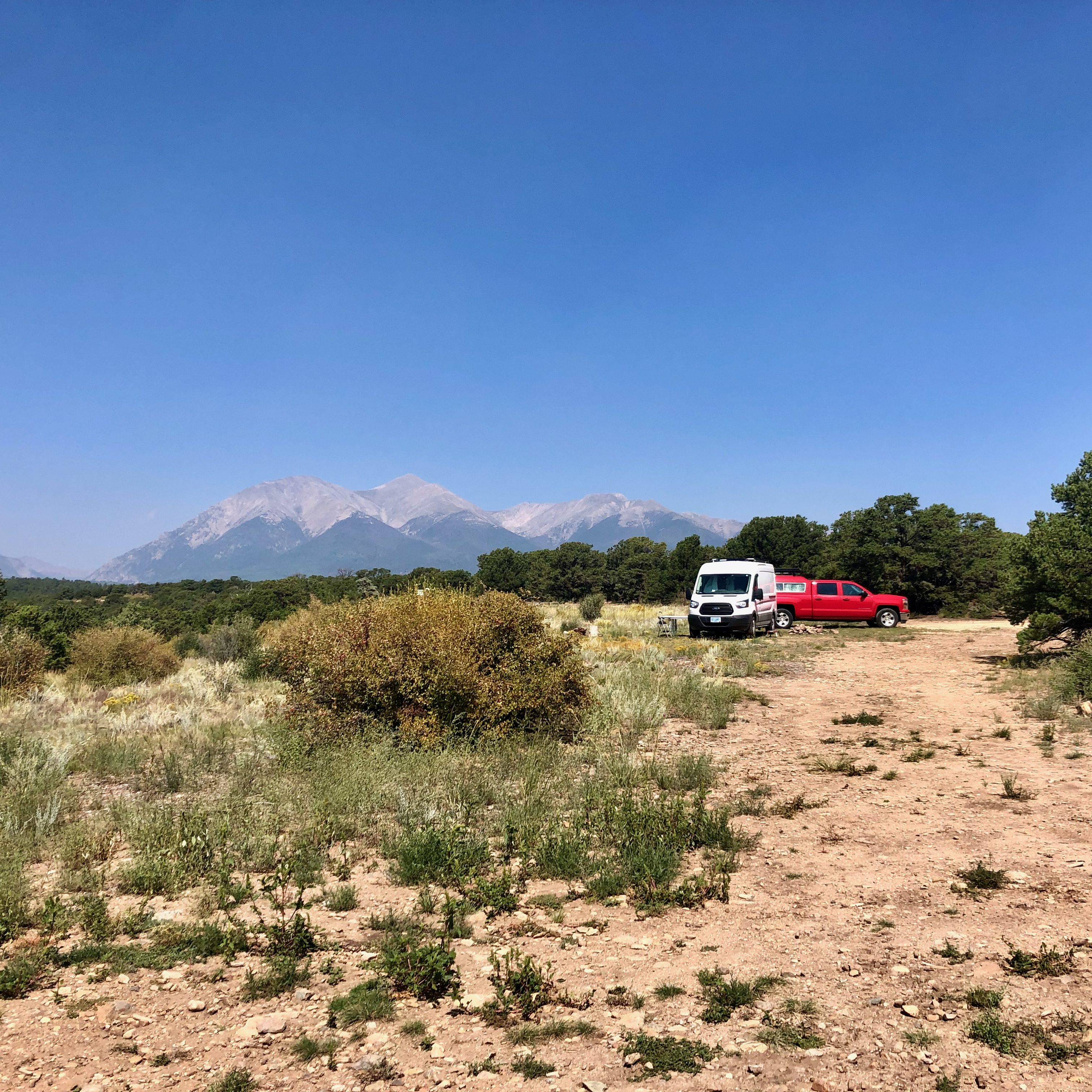 red truck and white van parked in short grass with mountains in the background on a clear blue day