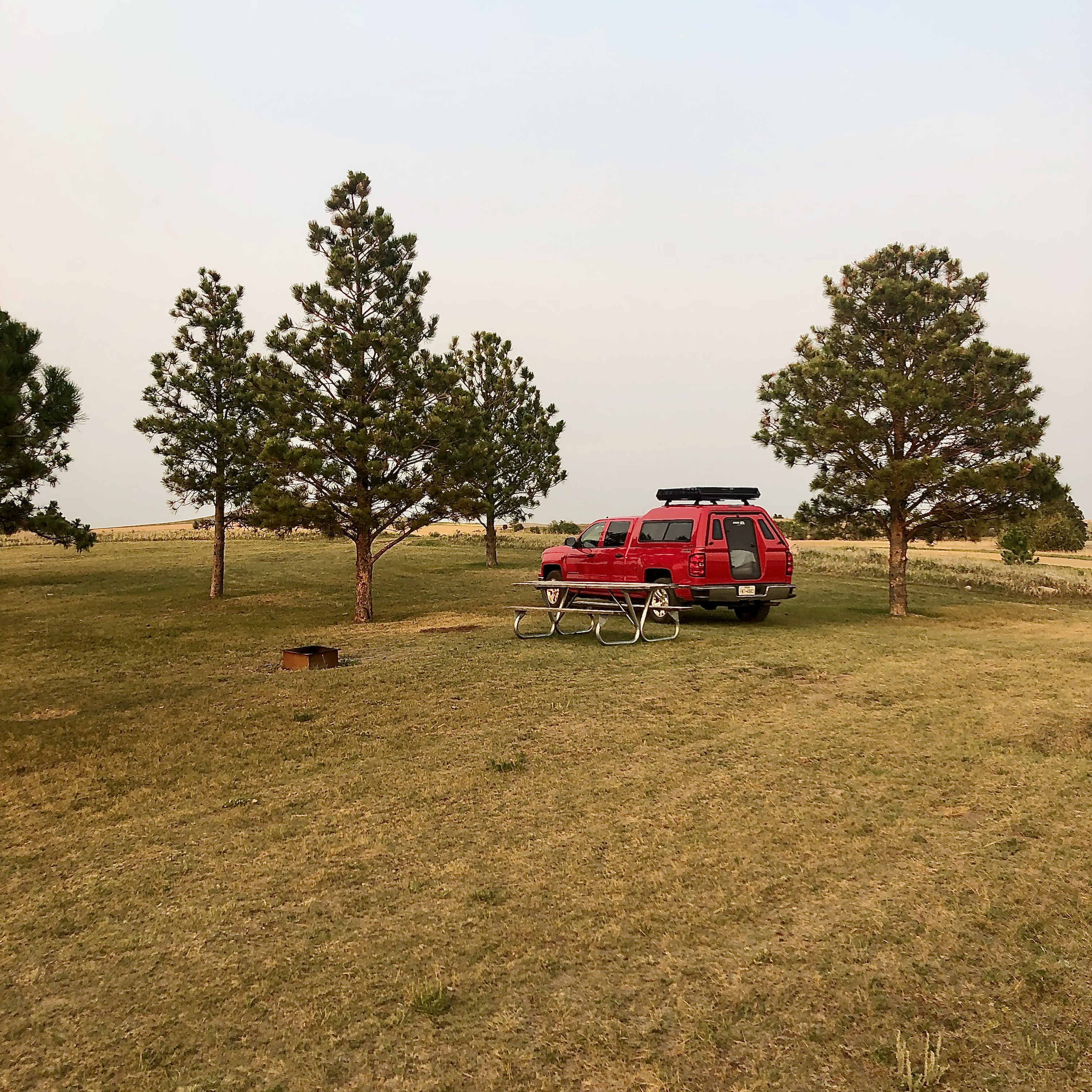 a red truck and a few green trees with brown grass at a campsite in Sweet Briar Dam State Game Management Area