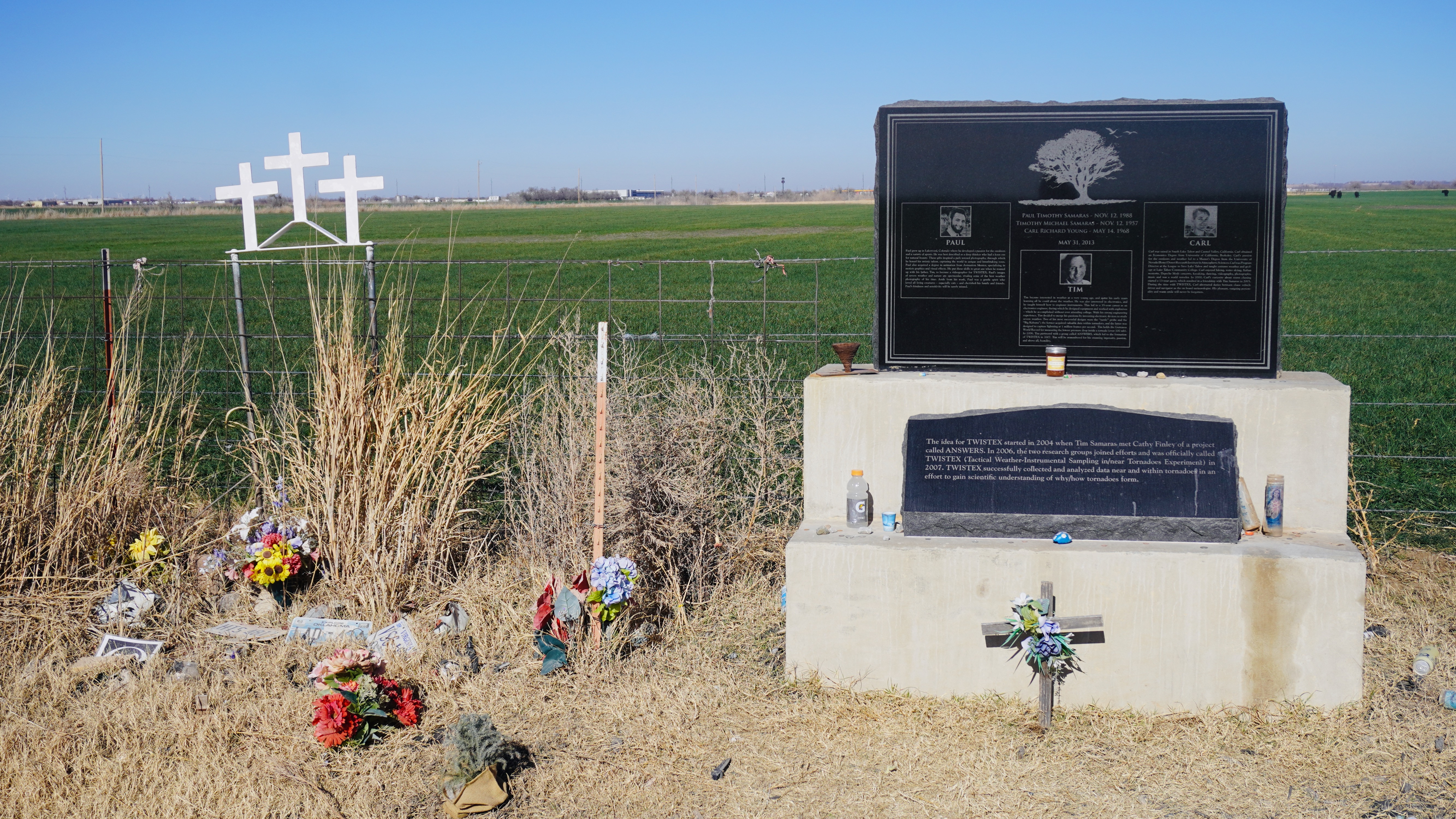 a black marble stone with writing about the people who were killed in the 2013 el reno oklahoma tornado with a green field behind it