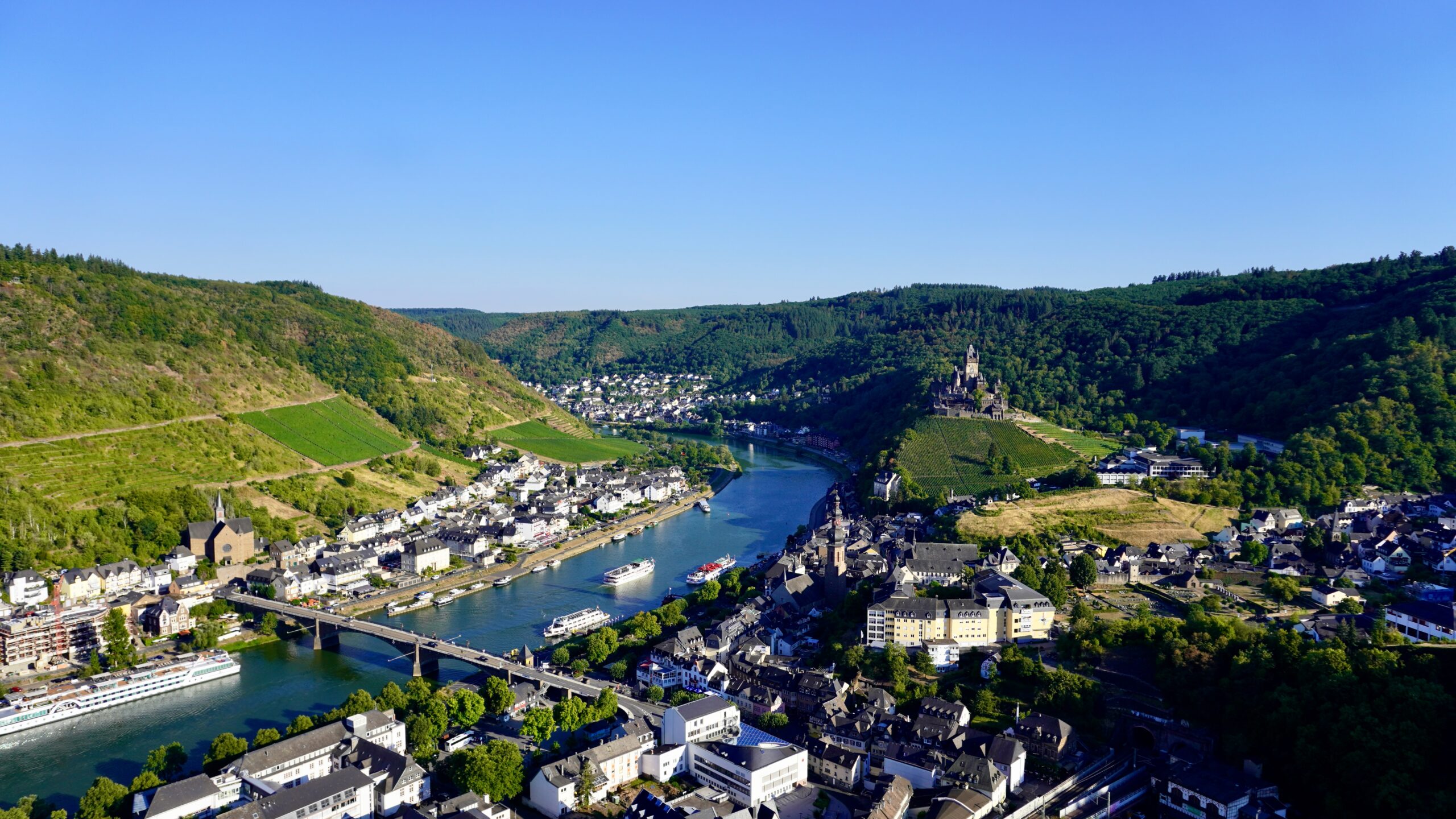 a city view of cochem from the hills showing the river, city, and castle in the moselle wine valley