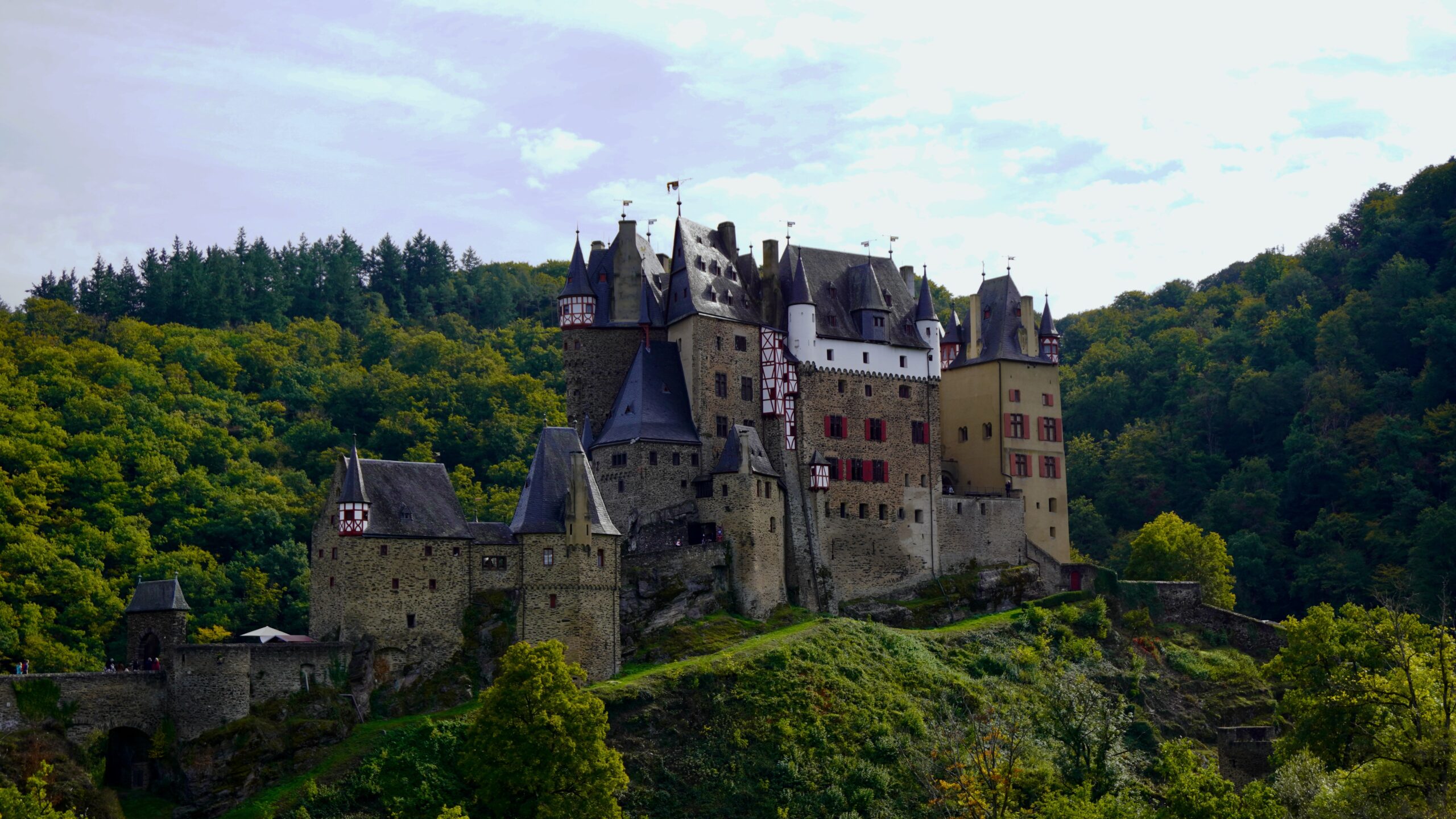 burg eltz castle with the forest and hill in the center with stone walls and some red and white timber rooms on top