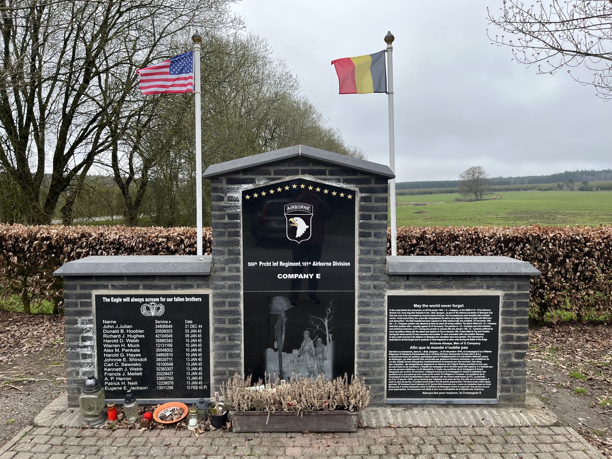 a grey brick stone memorial with black smooth granite with writing and pictures of the 101st eagle on the middle, names on the left, and history on the right with green fields behind