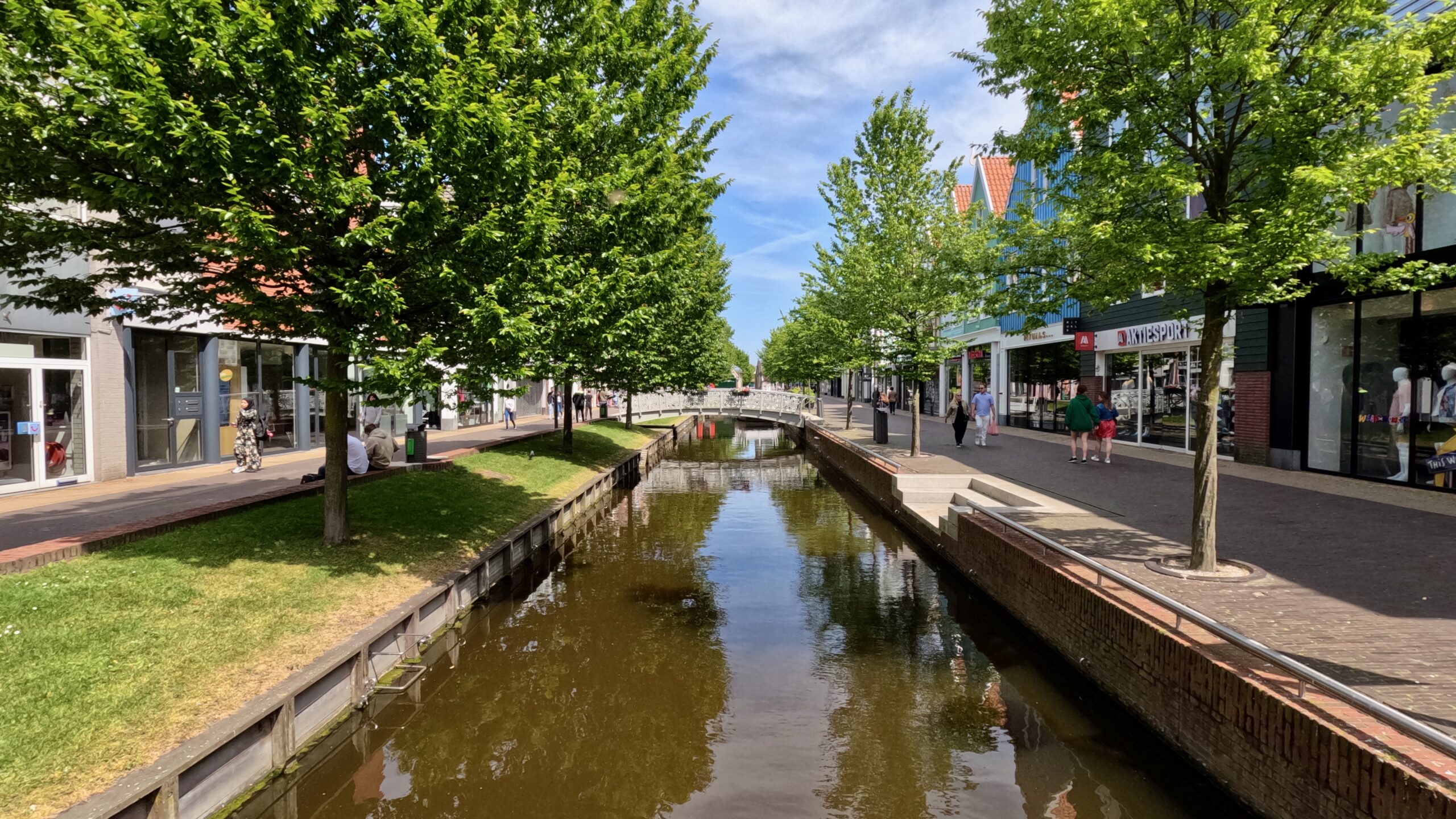 a narrow canal with sidewalk and shops on both sides near Amsterdam