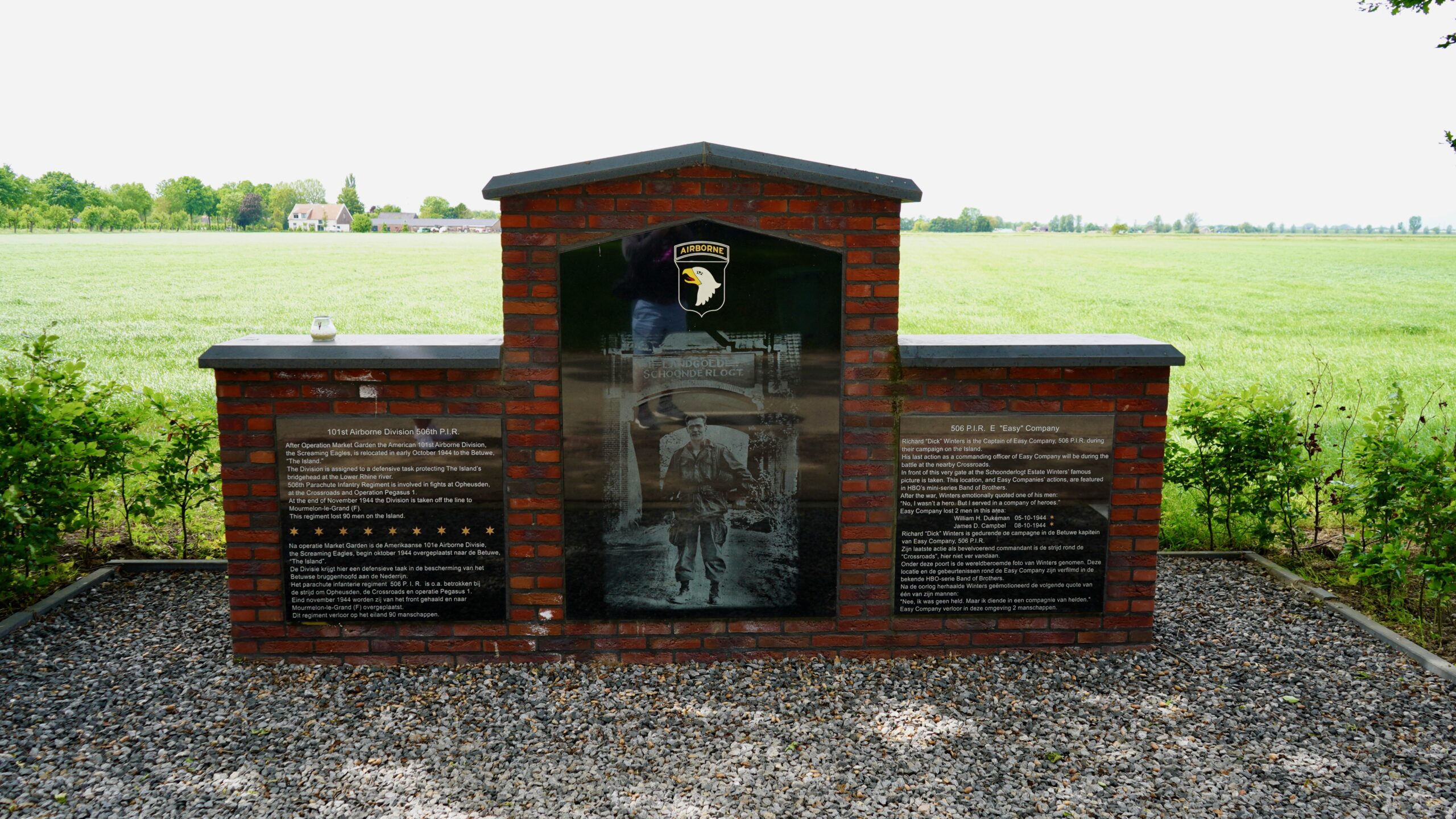 a brick memorial with black parts with writing and the picture of Dick Winters in front of the Schoonderlogt Farm