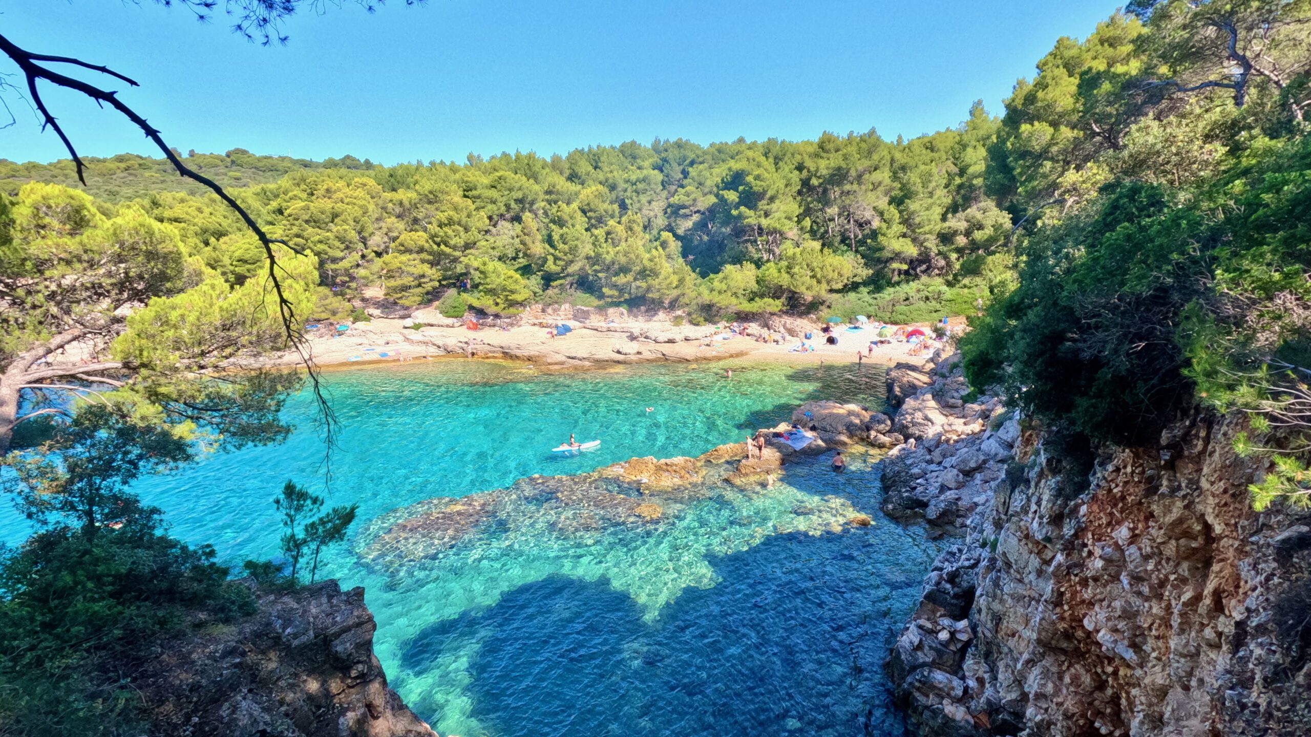 a blue green water with cliffs and trees next to a rocky pula beach