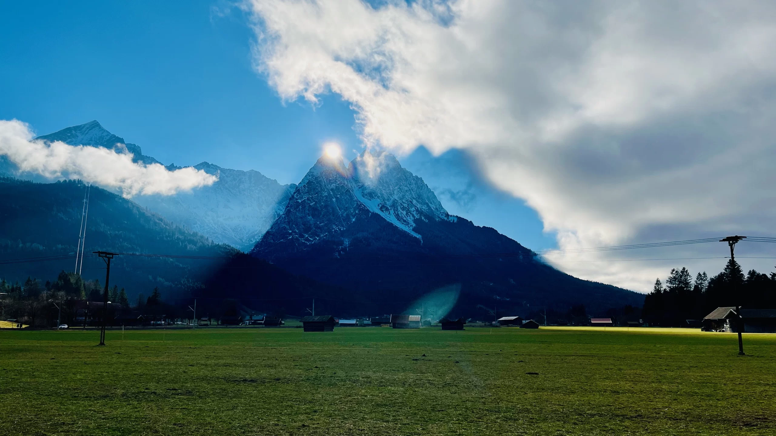 a pointy german alp mountain with the sun setting right at the top point of the mountain creating a high contrast shadow