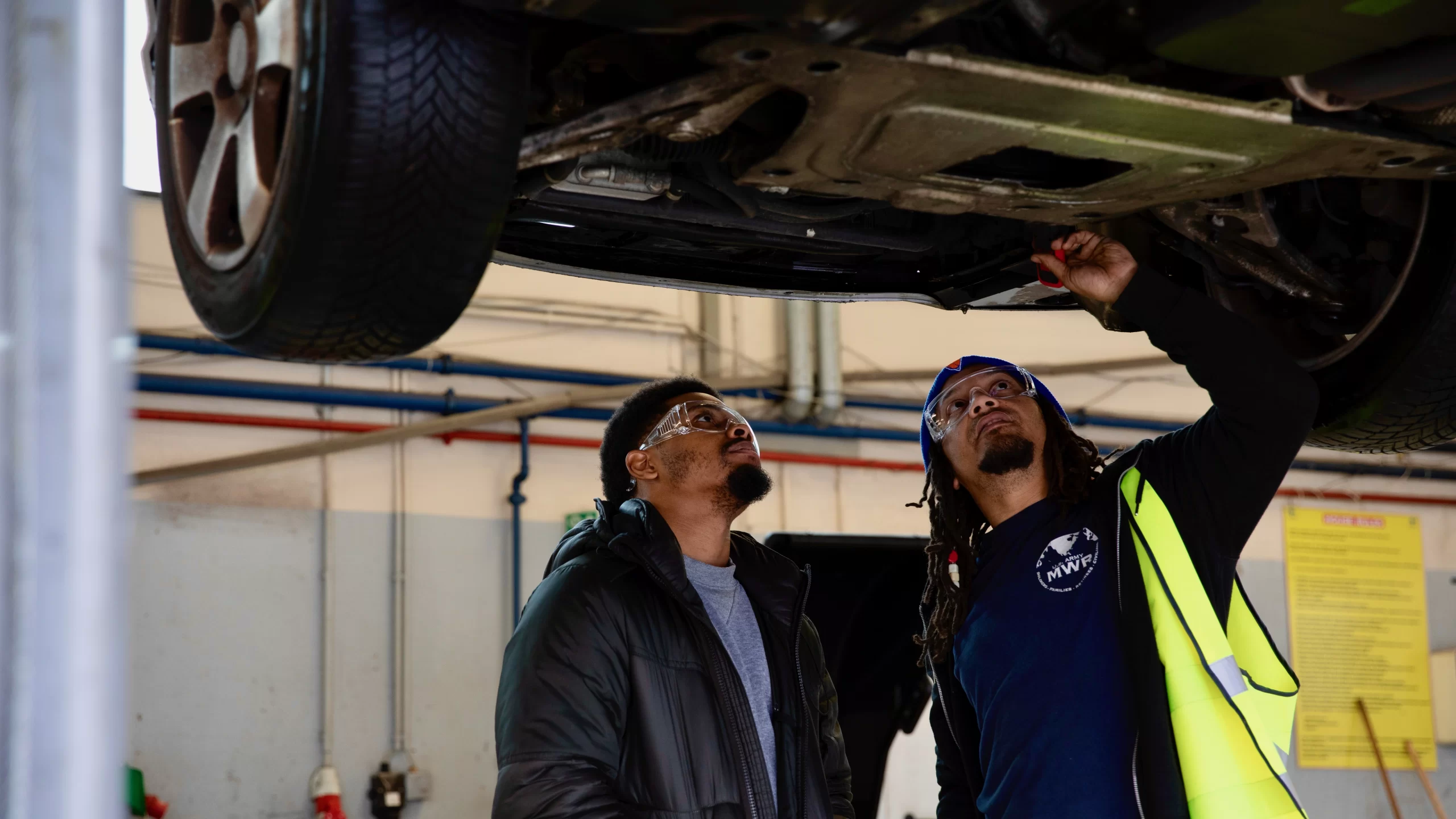 two men inspecting the underside of a vehicle